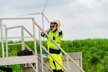 Worker in safety gear conducts maintenance near wind turbines in a green field on a cloudy day