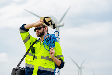 Worker in high-visibility clothing adjusts helmet near wind turbines during overcast day