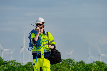 Construction worker in high visibility gear communicates on radio near wind turbines during the day