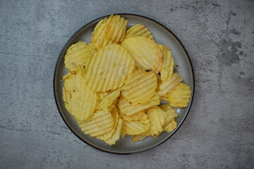 Potato Chips on a plate. Grey stone background. Top view. Copy space.