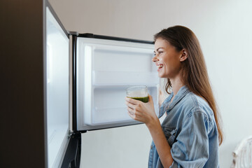 Happy woman enjoying healthy green smoothie in refrigerator, promoting healthy eating and wellness...