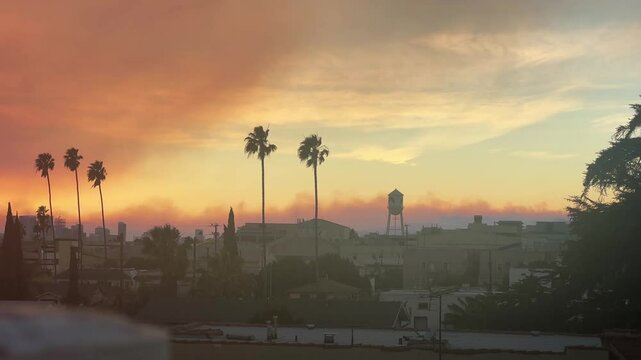 Handheld wide panning shot of the Palisades Fire burning in the distance as seen from a rooftop at sunset in Hollywood, California.