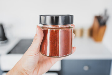 hand holding glass jar of smoked paprika in front of kitchen bokeh, cooking from scratch and having...