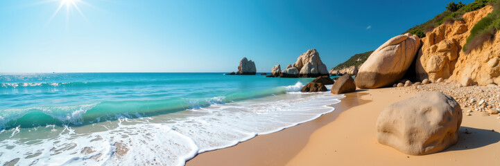 Obraz premium A picturesque sandy beach with clear blue water, large rocks, and cliffs under a sunny sky.