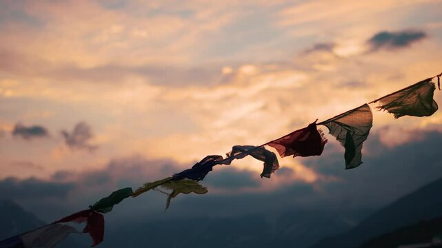 4K Slow motion shot of prayer flags waving in the wind in front of snowy Himalayan mountain peaks covered by clouds during the sunset at Khangsar village in Lahaul valley, Himachal Pradesh, India.