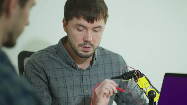 Two coders in a modern office engage in a productive discussion, sharing ideas on programming robotics arm with artificial intelligence.