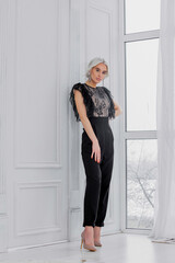 Fototapeta premium Young beautiful blonde model girl with hair and makeup in a fashionable black jumpsuit