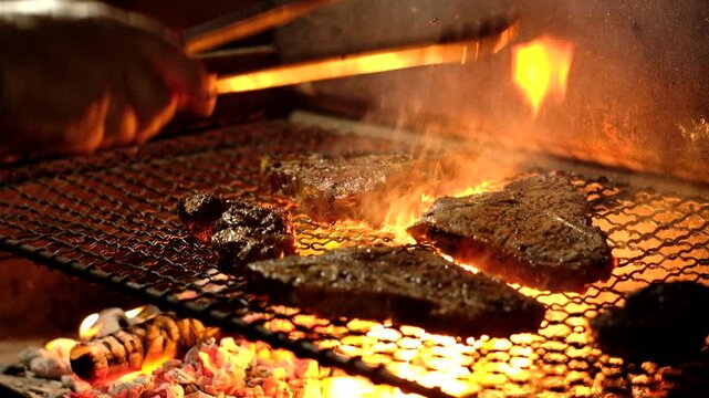 Tongs used to flip and grill juicy beef steaks on hot coals with licking flames