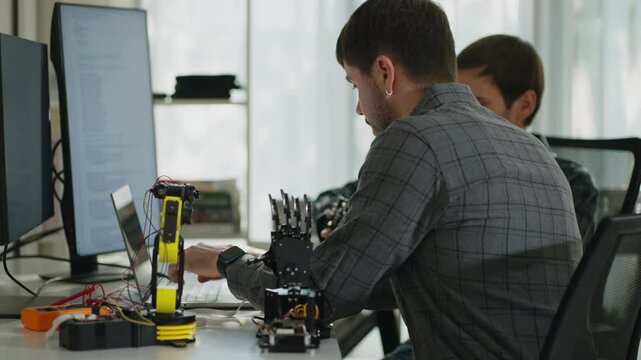 Two engineers connect through their work, typing code and leveraging advanced technology to solve the robotics arm problems in automated office.