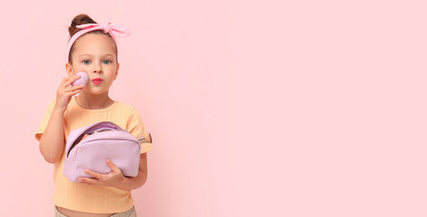 Cute little girl with makeup sponge and cosmetic bag on pink background