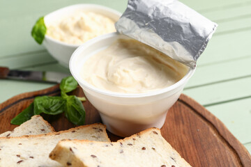 Plastic container with tasty cream cheese on green wooden background
