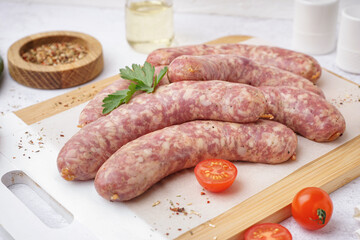 Wooden board with raw homemade sausages on light background