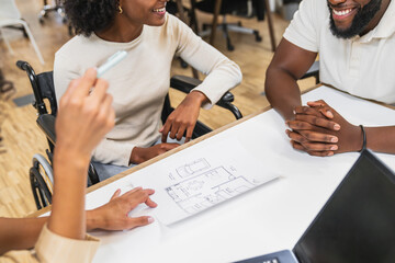 Architects discussing blueprint in coworking space, woman in wheelchair