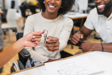 Real estate agent giving keys to happy couple in coworking space