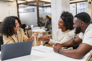 Real estate agent giving keys to happy couple in coworking space