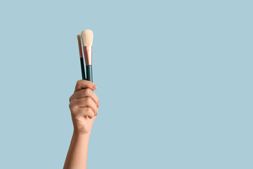 Female hand with makeup brushes on blue background