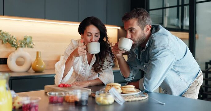 Smile, couple and drink coffee in kitchen with healthy food, nutrition fruits and morning breakfast. People, cheers and beverage with diet snacks for brunch, bonding together and marriage celebration