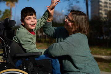 Happy child with disabilities giving high five to his educator in a park