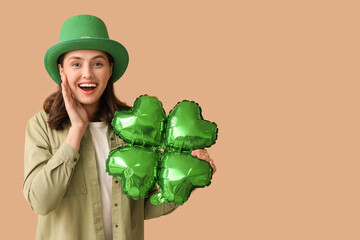 Happy young woman in leprechaun hat with air balloon in shape of clover on brown background. St....