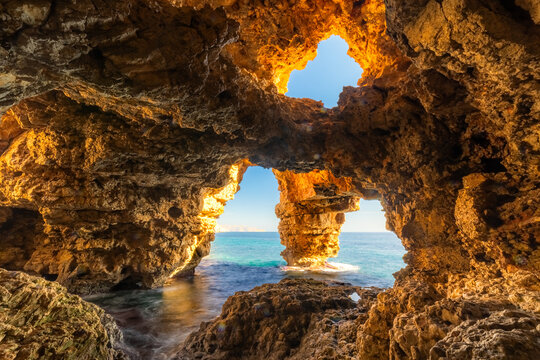 Sunlit sea cave with ocean view, rugged cliffs, and crystal waters, Cueva de Los Arcos, Moraig, Spain