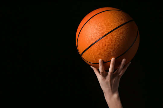 Young female basketball player with ball on black background