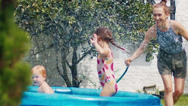 Family of mother and two kids have fun in the private pool in the green garden during summer hot day
