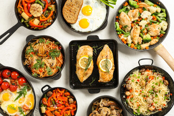 Frying pans with different tasty dishes on light background