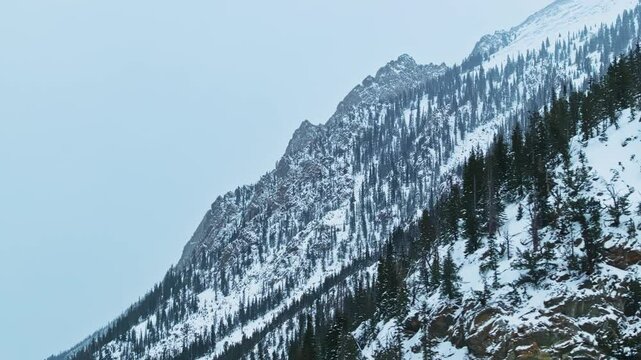 Aerial sweeping left reveals winter mountain landscape, jagged peaks and snow filled valleys below