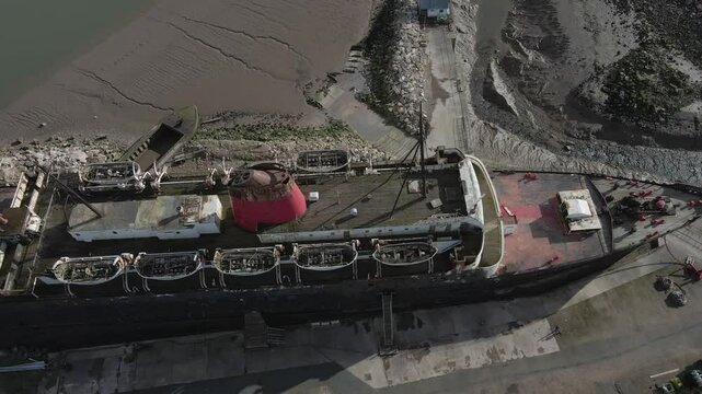 Aerial view of the Duke of Lancaster ship that is moored in the banks of the Welsh estuary, at Llanerch-y-mor. Drone moving to the left with camera facing down from the front of the ship to the back.