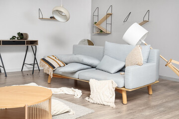 Sofa with overturned lamp in messy living room