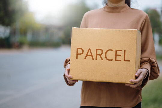 Woman holding a parcel box standing on the street, delivering the parcel to a location