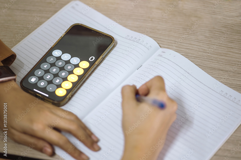 Poster smartphone with calculator app open, placed on a notebook while a person is writing