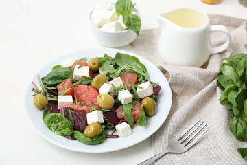 Plate of healthy vegetable salad with feta cheese, grapefruit, olives and basil on white table