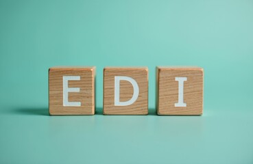 Three wooden blocks displaying EDI acronym for Electronic Data Interchange on teal background. Cubes symbolize data exchange, tech solutions, modern communication in digital world. Business concept