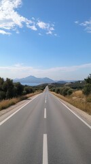 Obraz premium This image features a tranquil empty road stretching into the distance under a bright blue sky, framed by lush greenery and distant mountains.