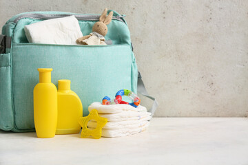 Baby bag with bottles of cream on table against grey background