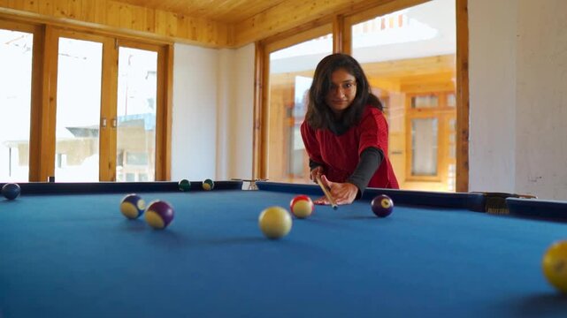 Indian woman playing pool game in resort and happy due to successful shot. Tourist enjoying holidays at Tirthan, Himachal Pradesh, India. Girl playing indoor game, enjoying hobby.
