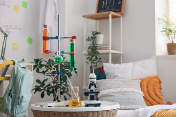 Modern microscope and chemical flasks on table in stylish teenager's room