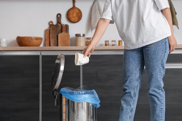 Woman throwing garbage into trash bin in kitchen