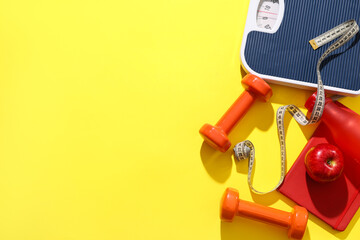 Scales with measuring tape, dumbbells and apple on yellow background. Weight loss concept