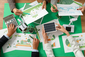 Business team with wind turbine models and solar panel working on green energy strategies during...