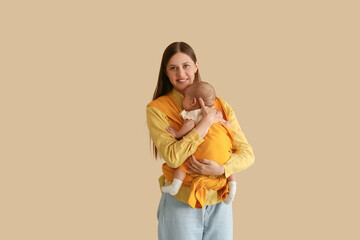 Young mother with little baby in sling on beige background