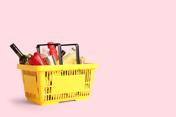Yellow shopping basket full of different fresh products and bell pepper on pink background