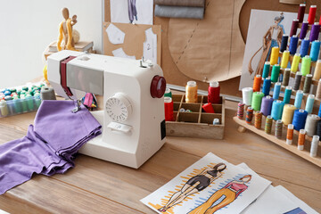 Sewing machine with cloth and thread spools on fashion designer's table in studio