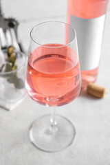 Glass, bottle of pink wine, cloth and corkscrew on table against white background