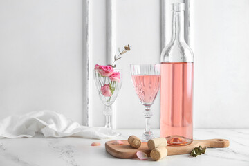 Bottle and glass of pink wine on board with corks on table against white background