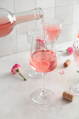 Pouring pink wine from bottle into glass on table against white tile background