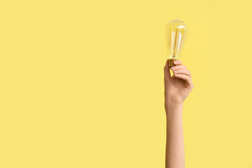 Female hand with tear-shaped light bulb on yellow background