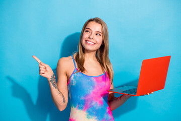 Stylish young woman with long hair holding a colorful laptop posing against a bright blue background