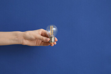 Female hand with round light bulb on dark blue background